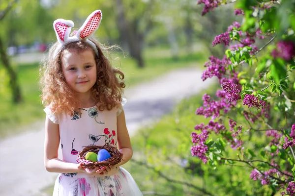 Girl holding a basket with painted Easter eggs. The child gathered on the street in the spring of eggs from the Easter Bunny. Cute little child wearing bunny ears on Easter day.