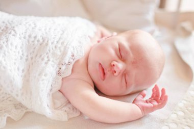 Küçük bebek dantelli battaniyeye sarılı beyaz bir beşikte uyuyor. Sağlıklı küçük çocuk elini kaldırdı. Kapalı bebek gözleri.