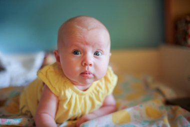 Sarı elbiseli bir bebek dairedeki bir soyunma masasında yatıyor. Küçük bebek kendinden emin bir şekilde elini tutuyor. İlk çocuk becerileri. Aylarca çocuk gelişimi. Hayatın ilk ayı sağlıklı bebek. Seçici odak