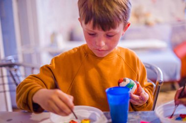 Çocuk Paskalya yumurtasını gökkuşağının renkleriyle süslüyor. Çocuk bir yumurta tutuyor ve onu fırçayla boyuyor. Paskalya kutlaması için hazırlanıyor. Film tahılı. Boşluğu kopyala