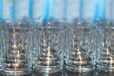 A row of empty glasses for vodka. Small piles for water. Banquet preparation.