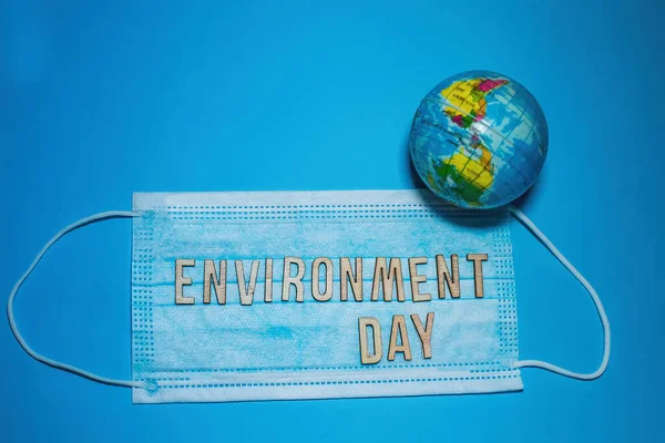 Word ENVIRONMENT DAY of wooden letters against background of protective medical mask. globe model Earth on blue background. Environmental protection concept.