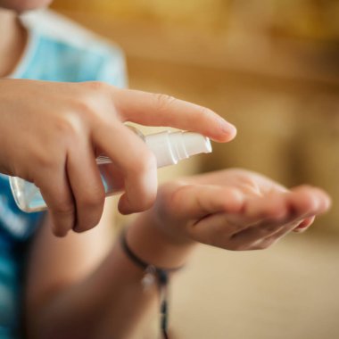 Çocuk, virüslerin cildini tedavi etmek için antibakteriyel sıvı için sprey sıkıyor. Koronavirüsten koruma. Enfeksiyonu önlemek için el dezenfektanı kullanın.