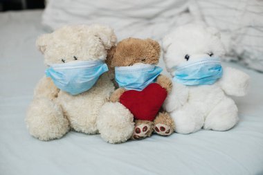 Yatağında koruyucu tıbbi maskeleri olan kırmızı kalpli üç oyuncak ayı. Çocuklarda daha hastalıklı bir hastalık. Koronovirüs, karantina, salgın, salgın, soğuk, hastalık. Tıp konsepti ve sağlık.