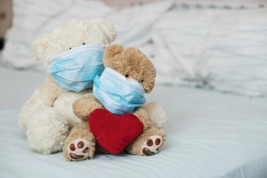 Yatağında koruyucu tıbbi maskeleri olan kırmızı kalpli iki oyuncak ayı. Çocuklarda daha hastalıklı bir hastalık. Koronovirüs, karantina, salgın, salgın, soğuk, hastalık. Tıp konsepti ve sağlık.