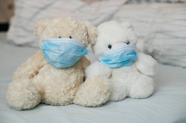 Yatakta tıbbi maskeli iki oyuncak ayı. Çocuklarda daha hastalıklı bir hastalık. Koronovirüs, karantina, salgın, salgın, soğuk, hastalık. Tıp konsepti ve sağlık