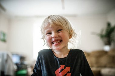 A happy, young girl with blonde hair smiles directly at the camera.