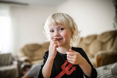 A small girl in a devil costume dances playfully with brother in the background.