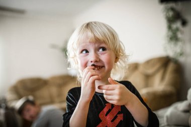 A small girl in a devil costume dances playfully with brother in the background.