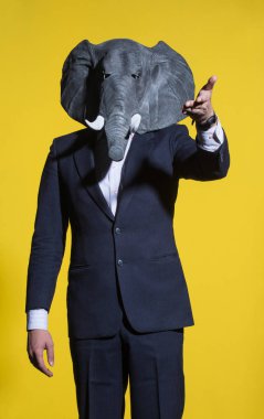 A man in a suit and an elephant mask on a yellow background. Conceptual business background clipart