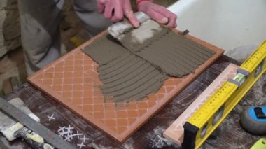 İşçi fayans üzerinde çimento yapıştırıcı uygular. Bitirme işleri, ellere odaklan. Kiremit döşeme teknolojisi.
