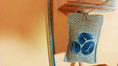 Üç koyu mavi kahve çekirdeği ile desenli bir iple asılmış küçük bir çuval turuncu duvara dekorasyon veya doğal koku giderici olarak bağlanır..