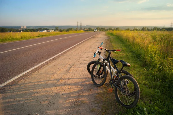 Bicycle tourism. Mountain bikes on a sunny evening at the edge of the road, fields and landscape. Active rest on vacation.