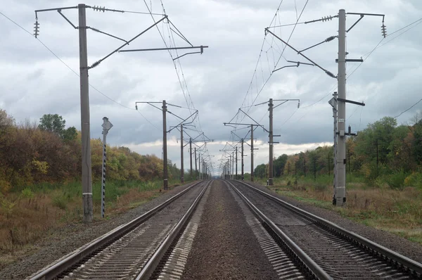 秋の鉄道線が地平線を越えて伸びる。重い鉛のような空の下で曇り 10 月の産業景観 — ストック写真