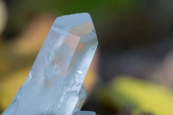 Kvartskristall på bakgrund av höst lövverk. Vacker pärla chalcedony — Stockfoto