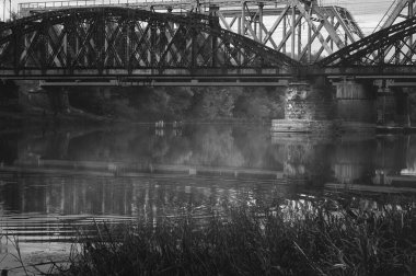 Sonbahar sisli nehir üzerinde eski demiryolu köprüleri siyah ve beyaz görüntü. Kasvetli atmosferik şehir manzarası