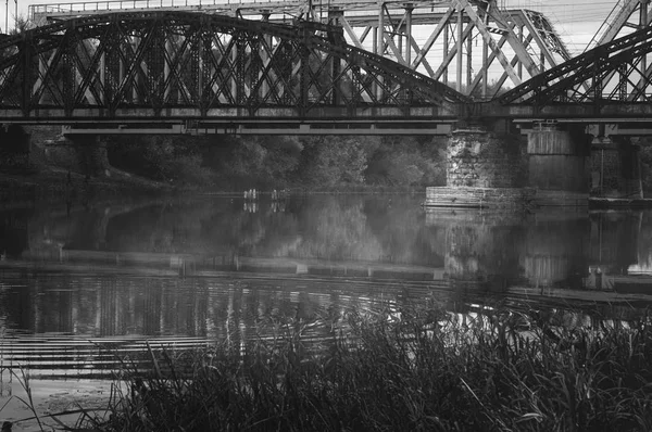 Zwart-wit beeld van oude spoorbruggen over de herfst mistig River. Sombere atmosferische Cityscape — Stockfoto
