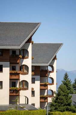 Bulgaristan 'ın Bansko kentindeki modern otel / konut binası. Özellikler çatıları, kemerli pencereleri ve çiçek kutularıyla dolu balkonları gösteriyordu. Gökyüzü açık, dağlar uzak. (177 karakter)