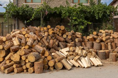 Büyük bir ham odun koleksiyonu ve düzgünce ayrılmış yakacak odun zeminde toplanıyor. Bu büyük yığın yeşil sarmaşıklarla süslenmiş bir binaya karşı kurulmuş. Bu da yakıt hazırlığı olduğunu gösteriyor..