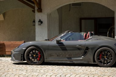 Koyu gri Porsche 718 Boxster Spyder kaldırım taşlarının üzerinde. Yan görüş: sportif tasarım, siyah tekerlekler, kırmızı kalibreler. Klasik bina arkaplanı.