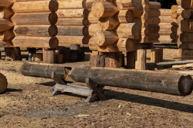 Kütük ahşap duvarları ve ön planda büyük bir kütüğü olan bir inşaat alanı. Kırsal, el yapımı ahşap bir ev inşa etmenin karmaşık sürecini gösterir.