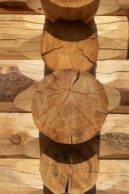 Yakın plan: Birbirine kenetlenmiş kütükler bir köy evi köşesi oluşturuyor. Doğal ahşap tanecikler, yıllık halkalar ve çatlaklar görünür, güneş ışığı / gölgelerle vurgulanır, geleneksel kereste yapısını gözler önüne serer..