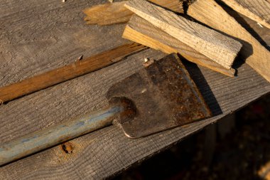 Eski, paslı bir el aleti, ahşap kırıntıların yanında eski ahşap bir yüzeye uzanır. Bu da ahşap bir ev ya da kırsal bir yapı inşa etmek için el emeğini ve malzeme hazırlığını sembolize eder..