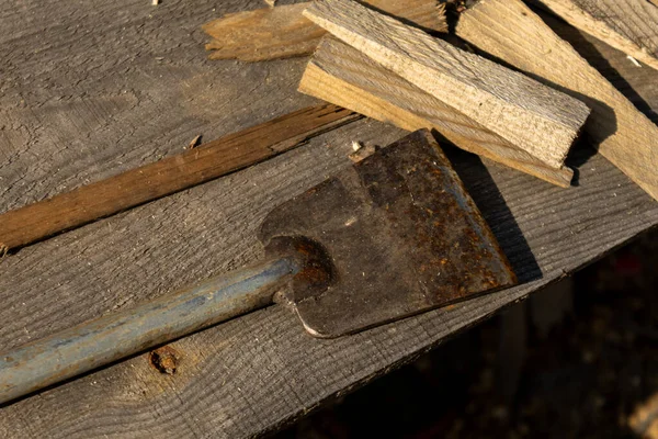 Eski, paslı bir el aleti, ahşap kırıntıların yanında eski ahşap bir yüzeye uzanır. Bu da ahşap bir ev ya da kırsal bir yapı inşa etmek için el emeğini ve malzeme hazırlığını sembolize eder..