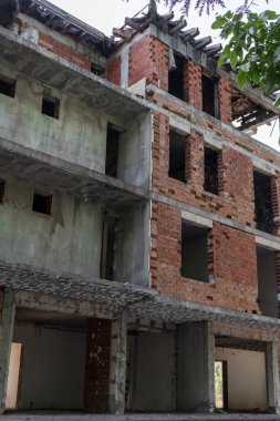 Çok katlı terk edilmiş bir binanın alçak açılı görüntüsü, inşaatın ortasında durmuş. Açığa çıkan kırmızı tuğla & ham beton ihmal, başarısız projeler ve ekonomik kriz çağrıştırıyor.