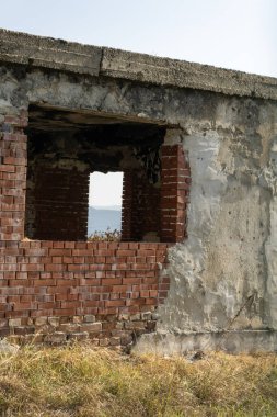 Parlak bir gökyüzünün altında kırık tuğlaları ve betonu olan yıpranmış, terk edilmiş bir bina. Boş pencere çerçeveleri dingin, uzak manzara, çürümeyi vurgulayan doğa.