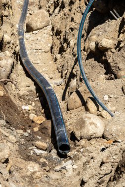 Kayalık bir hendekte mavi çizgili siyah plastik boru (HDPE ve PEX su borusu). İnşaat alanı yeraltı hizmetleri.