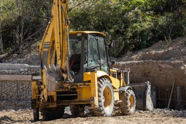 Güçlü bir sarı kepçe doldurucu, yeni ev inşaatı sırasında zemin çalışması ve kazı için gerekli olan güneşli bir şantiyede çalışmaya hazır bekliyor..