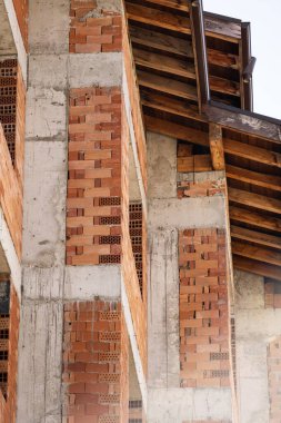 Devam eden modern ev inşaatı: beton sütunlar, kirişler, kırmızı tuğla dolgu. Ev yapımında kullanılan malzeme ve teknikleri vurgular.