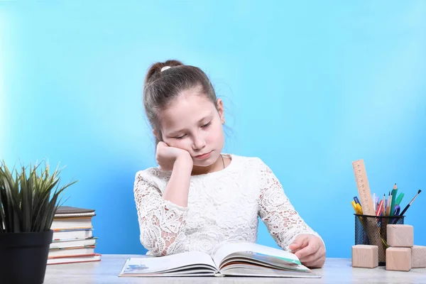 Back to school .Happy cute industrious child is sitting at a desk indoors.The girl reads a book and is sad.Kid is learning in class.quarantine.Kid is learning in home