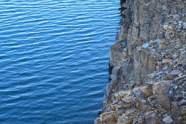 Stone rocks near water, on the background of lake, river, sea, ocean. Blue clear water. Artificial water reservoirs.