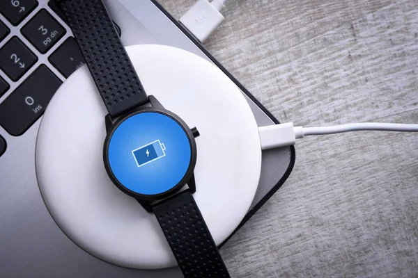 Smart watch on wireless charging with on-screen charging indicator. At the desktop, near at the laptop. Top view. Place for text