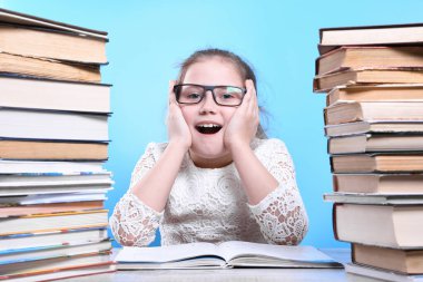 Okula geri dönen mutlu, çalışkan çocuk kapalı bir masada oturuyor. Çocuk sınıfta öğreniyor. Kenarlarında kitap dağları var.