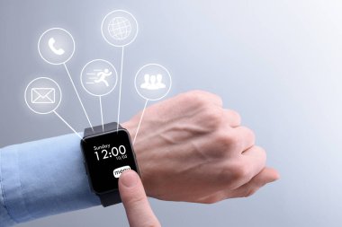 Bir iş adamının elindeki akıllı saat. Adam menüde farklı simgeler arasında telefon, mesaj, bağlantı, küresel ağ seçer