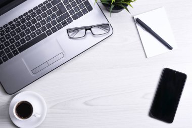 Ofis çalışma alanının en üst görüntüsü, dizüstü bilgisayarı, klavye kalemi, gözlükleri, telefonu, defteri ve kahveyi olan ahşap masa masası..