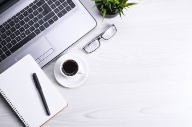Ofis çalışma alanının en üst görüntüsü, dizüstü bilgisayarı, klavye kalemi, gözlükleri, telefonu, defteri ve kahveyi olan ahşap masa masası..