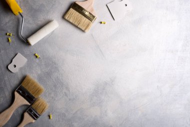 Gri beton arka planda boya yapmak için macun, fırça ve silindirler kullanılıyor. Üst görünüm
