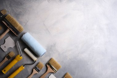 Gri beton arka planda boya yapmak için macun, fırça ve silindirler kullanılıyor. Üst görünüm