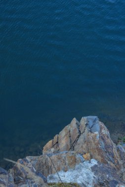 Su kenarındaki kayalar, gölün, nehrin, denizin ve okyanusun arka planında. Mavi berrak su. Yapay su rezervleri.