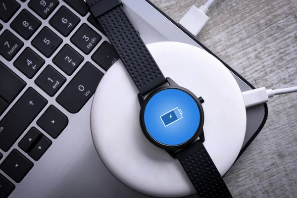 Smart watch on wireless charging with on-screen charging indicator. At the desktop, near at the laptop. Top view. Place for text