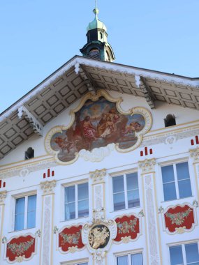 06.09.2025 Almanya: Geleneksel Bavyera Rathaus 'un Bad Toelz' deki beyaz cephesini detaylı freskler, sıva süslemeleri ve mavi gökyüzü altında dekoratif kırmızı elementlerle inşa ediyor.