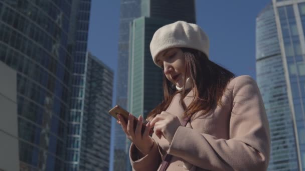 Mujer con el teléfono en el fondo de edificios altos de una megaciudad — Vídeo de stock