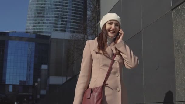 Женщина в пальто идет в центр города, разговаривает по телефону — стоковое видео