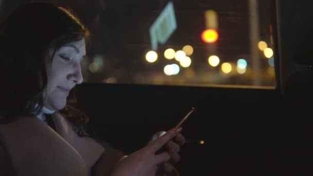 Beautiful woman in a passenger car seat with a phone rides in a night city — Stock Video