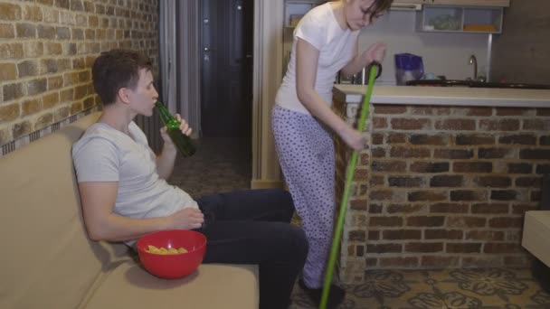 Дружина робить прибирання, перешкоджаючи чоловікові дивитися футбол — стокове відео