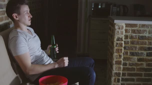 Jeune homme regarder la télévision avec de la bière et des chips — Video